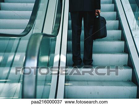 Stock Photo - Businessman on escalator, lower section, close-up, portrait.. Fotosearch