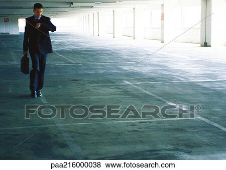 Businessman walking in parking garage, checking the time View Large Photo Image Stock Photo - Businessman walking in parking garage, checking the time. Fotosearch