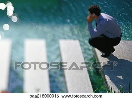 Man crouching near water, using cell phone. View Large Photo Image Stock Photography - Man crouching near water, using cell phone.. Fotosearch