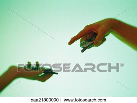 Stock Image - Two hands holding cell phones, one pointing down. Fotosearch