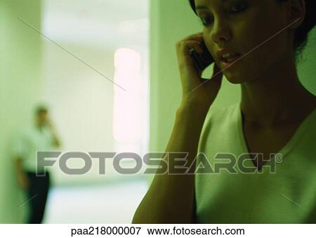 Woman using cell phone, man talking on cell phone in background View Large Photo Image Stock Photo - Woman using cell phone, man talking on cell phone in background. Fotosearch