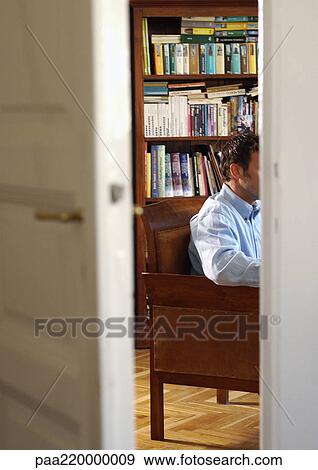 Man sitting in front of bookshelf, view through half-opened door View Large Photo Image Stock Photo - Man sitting in front of bookshelf, view through half-opened door. Fotosearch