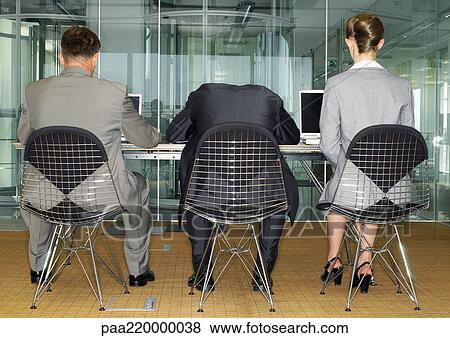 Stock Photo - Three people in suits, using laptops, one with head on table, rear view.. Fotosearch