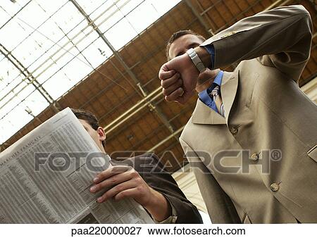 Two businessmen, one with newspaper, other checking watch, low angle. View Large Photo Image Stock Photo - Two businessmen, one with newspaper, other checking watch, low angle.. Fotosearch