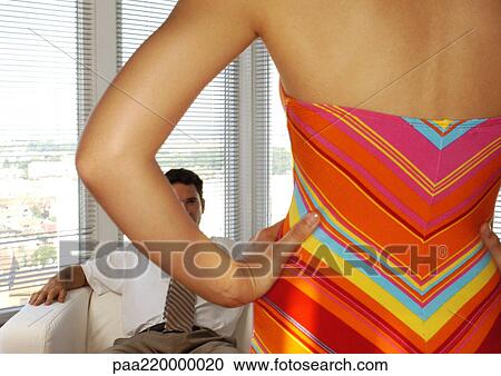 Stock Image - Woman standing in front of seated man, rear view.. Fotosearch