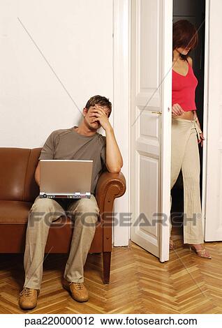 Young man using laptop, woman walking into room. View Large Photo Image Stock Image - Young man using laptop, woman walking into room.. Fotosearch