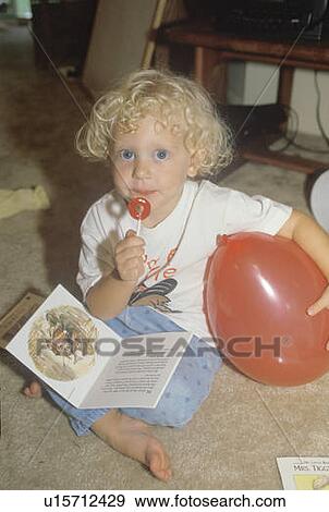 Stock Photo - A blonde child eating a lollipop at a daycare center. Fotosearch