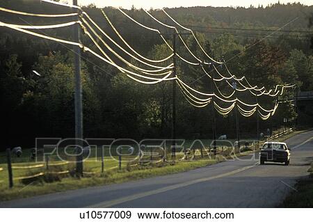 Stock Photo - A car driving down a road with power lines during sunset in Wheelock, Vermont. Fotosearch
