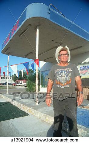 Picture - A man standing outside an abandoned gas station. Fotosearch