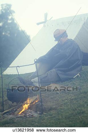 Stock Photo - Civil War confederate soldier participant by fire with tent in camp. Fotosearch