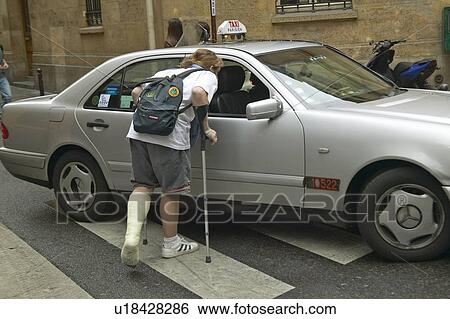 Stock Photograph - College boy with broken leg flagging down taxi. Fotosearch