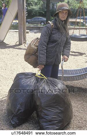 Stock Image - Elderly homeless woman holding possessions in garbage bags. Fotosearch