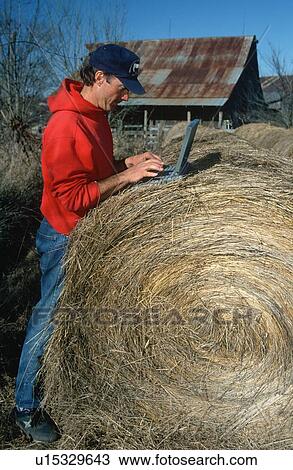 Stock Image - Farmer working on laptop computer on top of haystack. Fotosearch