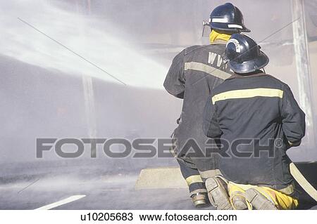 Stock Image - Firemen putting out a house on fire. Fotosearch
