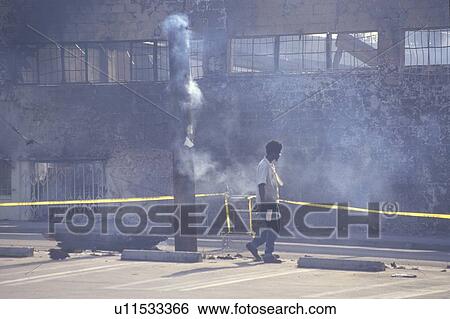 Stock Photograph - Man walking past burned industrial building after riots. Fotosearch