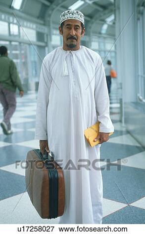 Middle Eastern man wearing white robes holding suitcase at airport View Large Photo Image Stock Photo - Middle Eastern man wearing white robes holding suitcase at airport. Fotosearch