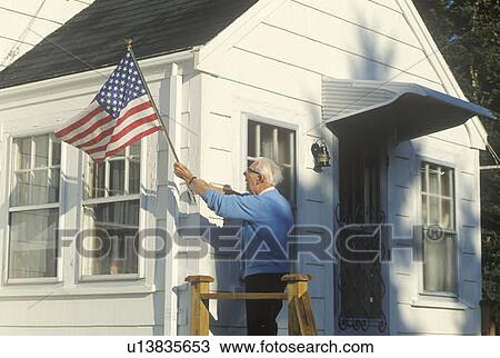 Stock Image - Old Man Putting American Flag on House. Fotosearch