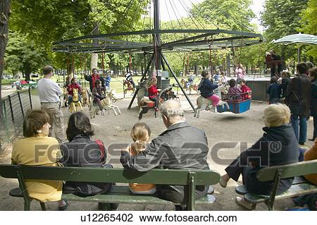 Stock Image - Parents and children at carousel ride in park, Paris, France. Fotosearch
