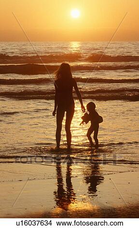 Silhouetted girl and child walking on beach at sunset View Large Photo Image Picture - Silhouetted girl and child walking on beach at sunset. Fotosearch