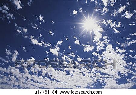 Picture - This is an image of altocumulus clouds with a sunburst. The surrounding sky is blue.. Fotosearch