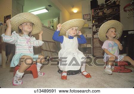 Stock Image - Three little girls wearing sombreros at their daycare center. Fotosearch