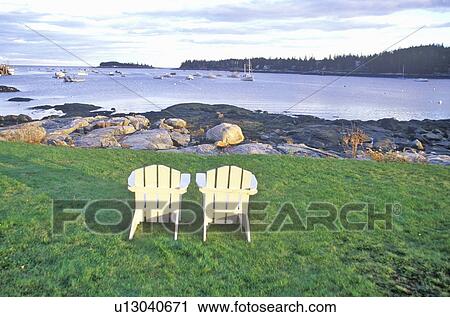 Stock Image - Two wooden lawn chairs set near the shore. Fotosearch