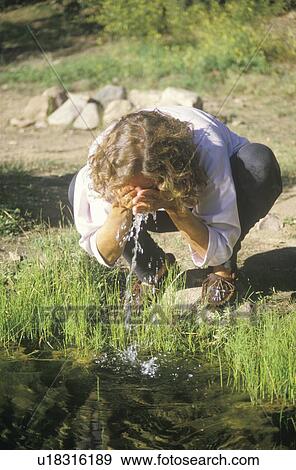 Stock Photo - Woman splashing some clean water on her face from a river. Fotosearch