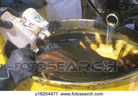 Stock Photo - Workers pouring toxic wastes into a metal drum at waste cleanup site on Earth Day. Fotosearch