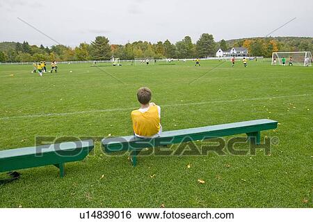 Stock Photograph - A boy rests on a bench during school soccer practice. Fotosearch