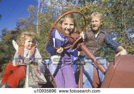 Stock Photograph - A father with his two daughters riding a tractor. Fotosearch