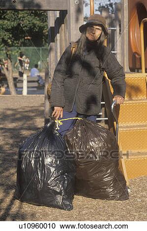 Stock Image - Elderly homeless woman holding possessions in garbage bags. Fotosearch