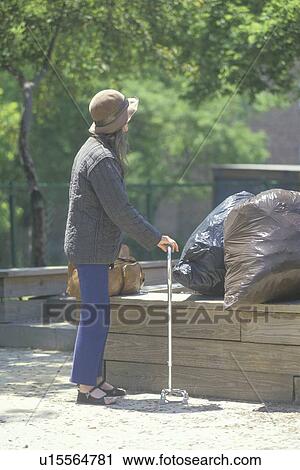 Stock Image - Elderly homeless woman walking with cane. Fotosearch