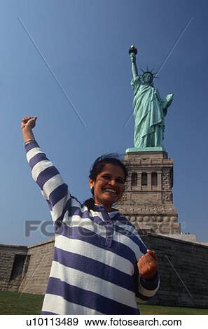 Stock Photo - Indian American woman raising arm, Statue of Liberty, New York. Fotosearch