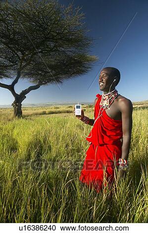 Stock Image - Masai Warrior near Acacia Tree listening to music. Fotosearch