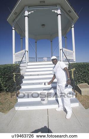 Stock Photograph - Painter paints Gazebo with new coat of white paint. Fotosearch