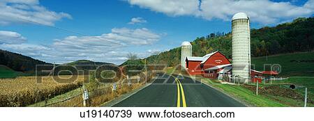 Stock Photo - This is a country road with a farm on the right hand side of the road. It has a red barn and silo. . Fotosearch