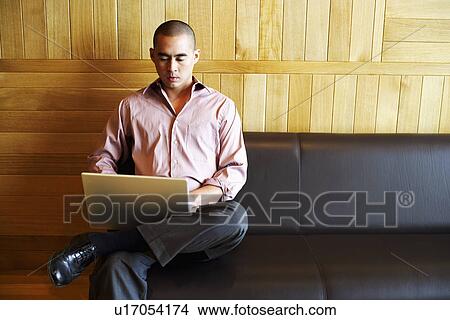 High angle view of a young man sitting on a couch and using a laptop View Large Photo Image Picture - High angle view of a young man sitting on a couch and using a laptop. Fotosearch