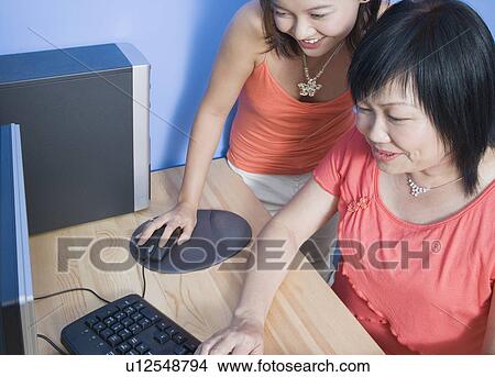 High angle view of a young woman and her mother using a computer and smiling View Large Photo Image Picture - High angle view of a young woman and her mother using a computer and smiling. Fotosearch