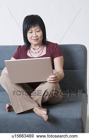 Mature woman sitting on a couch and using a laptop View Large Photo Image Stock Photo - Mature woman sitting on a couch and using a laptop. Fotosearch
