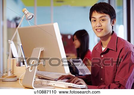 Stock Image - Portrait of a businessman sitting in front of a computer in an office and smiling. Fotosearch