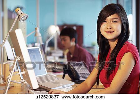 Portrait of a businesswoman sitting in front of a computer in an office and smiling View Large Photo Image Stock Photo - Portrait of a businesswoman sitting in front of a computer in an office and smiling. Fotosearch