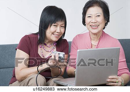 Portrait of a mature woman and a senior woman sitting with a digital camera connected to a laptop View Large Photo Image Stock Image - Portrait of a mature woman and a senior woman sitting with a digital camera connected to a laptop. Fotosearch