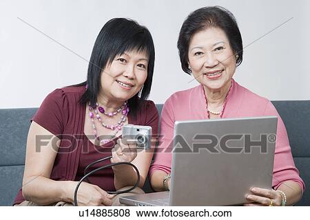 Portrait of a mature woman and a senior woman sitting with a digital camera connected to a laptop View Large Photo Image Stock Photo - Portrait of a mature woman and a senior woman sitting with a digital camera connected to a laptop. Fotosearch