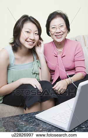 Stock Photo - Portrait of a senior woman with her granddaughter sitting on a couch in front of a laptop. Fotosearch