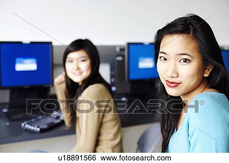 Portrait of two young women sitting in front of computers and smiling View Large Photo Image Stock Photograph - Portrait of two young women sitting in front of computers and smiling. Fotosearch