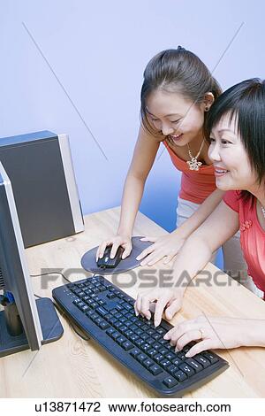 Stock Image - Side profile of a mature woman using a computer with her daughter standing beside her. Fotosearch