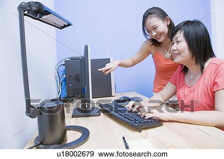 Side profile of a mature woman using a computer with her daughter pointing towards the monitor and smiling View Large Photo Image Stock Photo - Side profile of a mature woman using a computer with her daughter pointing towards the monitor and smiling. Fotosearch