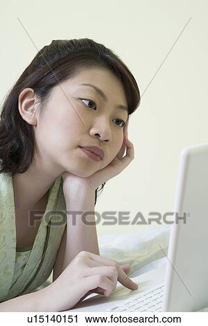 Side profile of a young woman lying on the bed and using a laptop View Large Photo Image Stock Image - Side profile of a young woman lying on the bed and using a laptop. Fotosearch