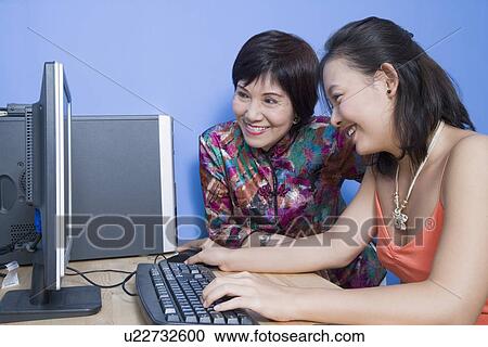 Side profile of a young woman using a computer with her mother sitting beside her View Large Photo Image Stock Image - Side profile of a young woman using a computer with her mother sitting beside her. Fotosearch