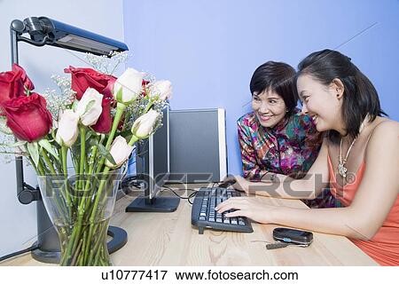 Stock Photo - Side profile of a young woman using a computer with her mother sitting beside her. Fotosearch